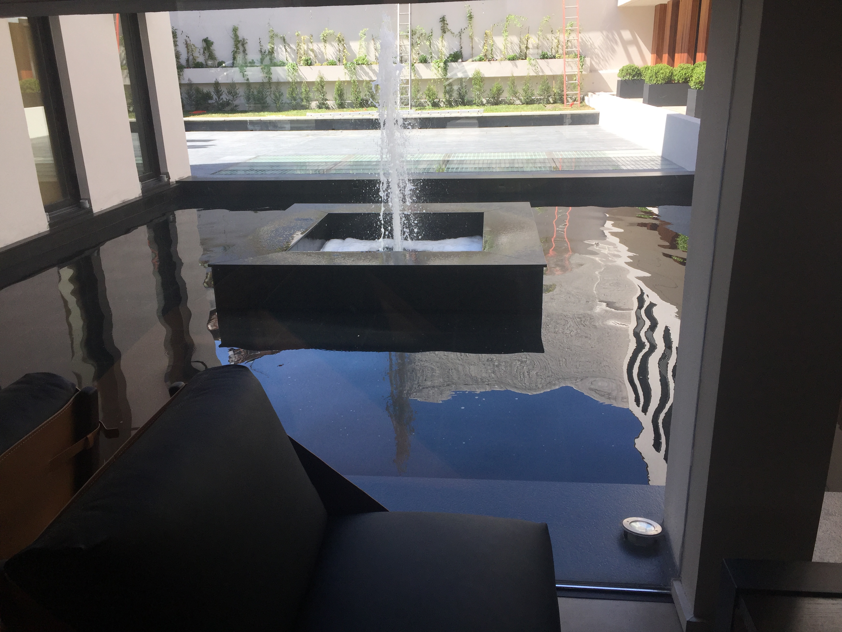 Es la fotografía de la fuente de agua que se encuentra en el patio principal del policlínico de blue cross ubicado en punta carretas. Está completamente revestida en granito negro, en el centro se encuentra cuatro muros revestidos en el mismo material con un chorro de agua ascendente, todo rodeado de un plato de agua de cinco metros de diámetro.